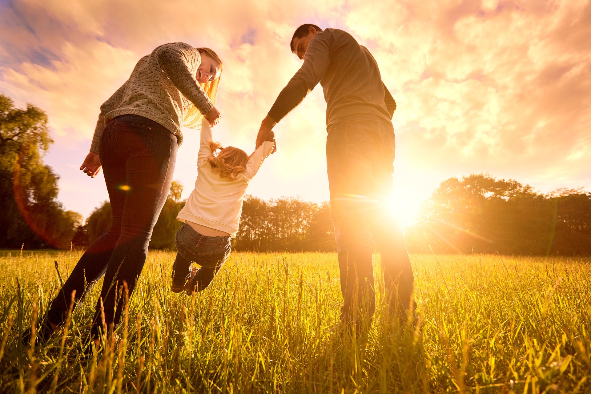 在公园晚上光的愉快的家庭。太阳的灯光。妈妈，爸爸和婴孩快乐步行在日落。一个幸福的家庭的概念。帕特斯抱着婴儿的手。